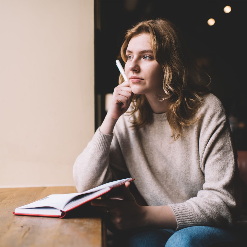 chica leyendo un libro en una mesa de madera con café y bloc de notas. concepto creativo de lector y escritor planificando su novela.
